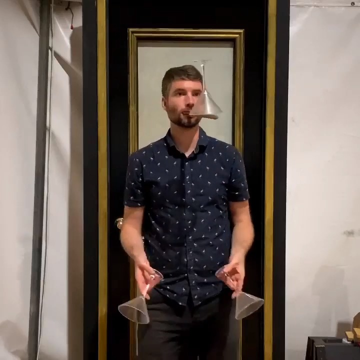 Performer Juggles Three Glasses And Balances Them On Top Of Mouth Stick