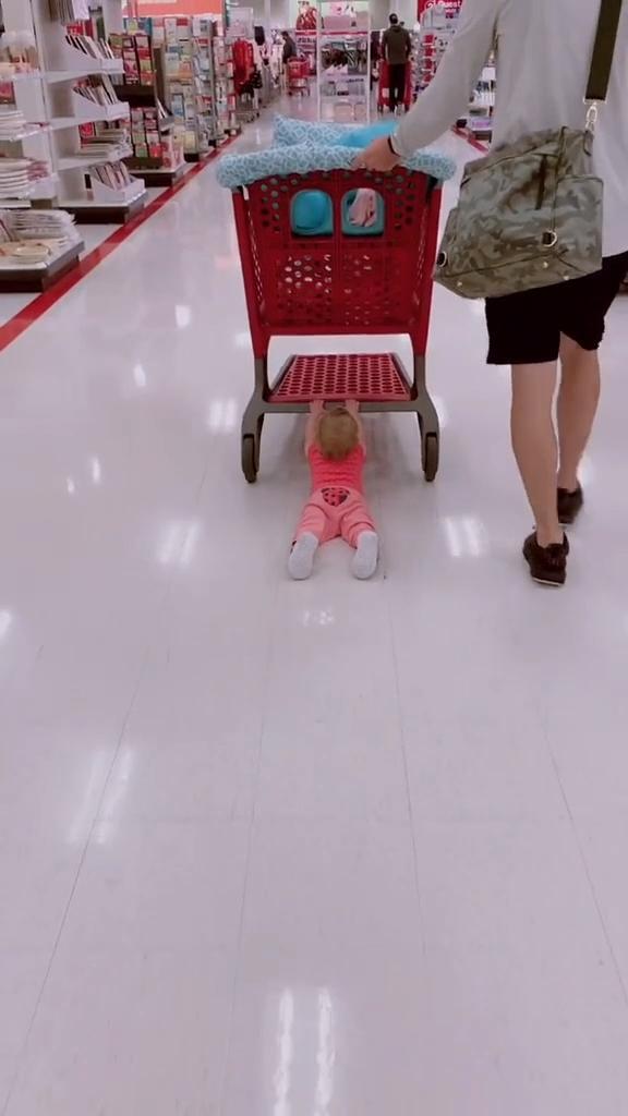 Toddler Lies on Floor Holding Shopping Cart Enjoying a Slide Ride as