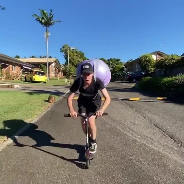 Guy Straps Exercise Ball to Back and Front Flips While Riding a Scooter