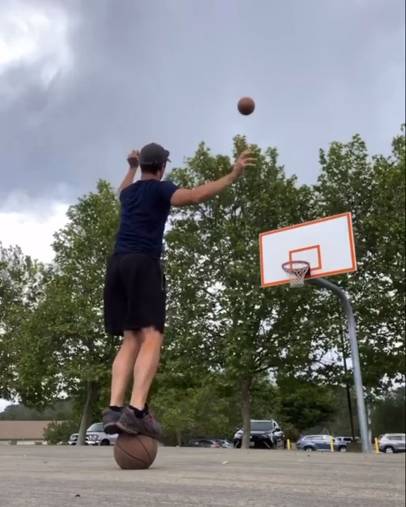 Guy Throws One Basketball in Basket While Standing Over Other and Makes